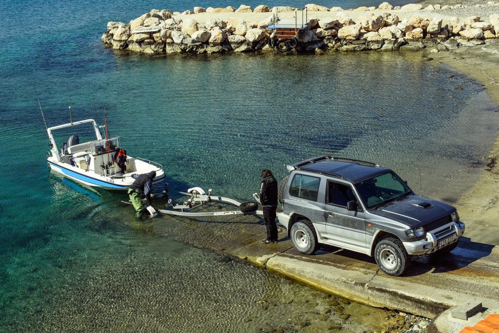Driver backing a boat trailer down a concrete boat ramp toward the water